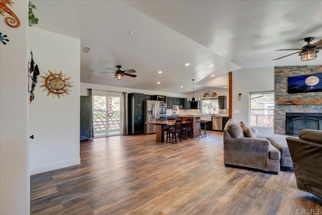 living area with a ceiling fan, a stone fireplace, wood finished floors, and lofted ceiling