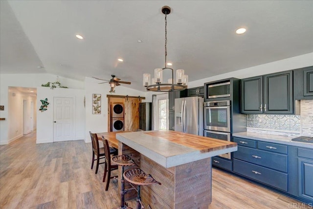 kitchen with a breakfast bar area, stainless steel appliances, a kitchen island, stacked washing maching and dryer, and vaulted ceiling