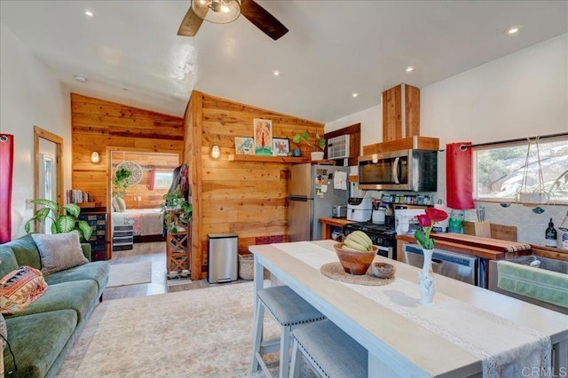 kitchen featuring a sink, wood walls, ceiling fan, stainless steel appliances, and open floor plan