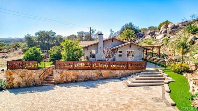 view of front of house with fence, stucco siding, and a chimney