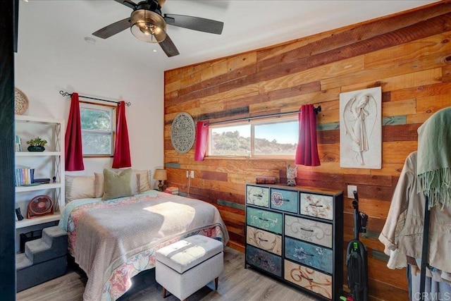 bedroom with wooden walls, multiple windows, ceiling fan, and wood finished floors