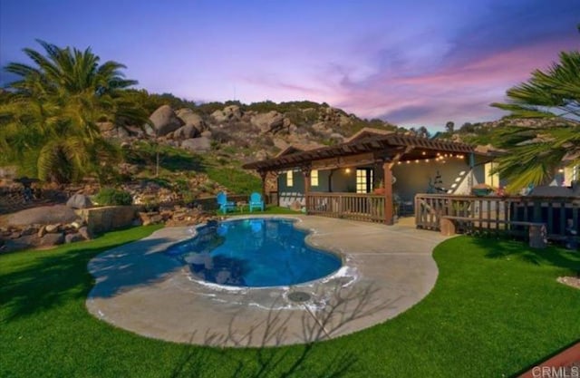 pool at dusk with a lawn, a pergola, an outdoor pool, and a patio area
