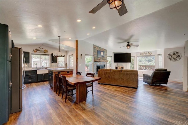 dining room with lofted ceiling, ceiling fan, recessed lighting, dark wood finished floors, and a stone fireplace