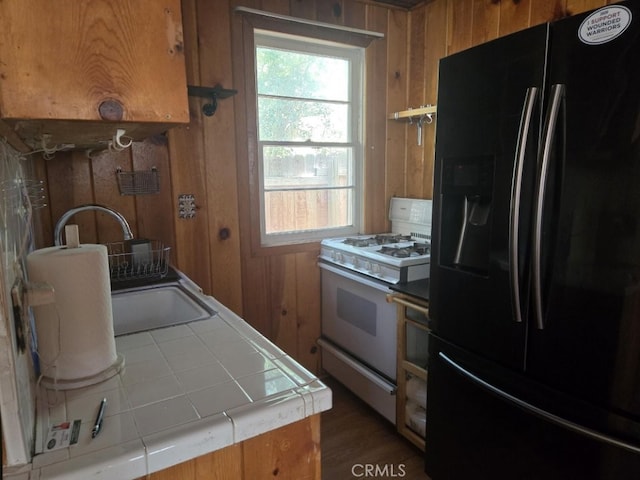 kitchen with tile counters, white gas stove, brown cabinetry, and black refrigerator with ice dispenser