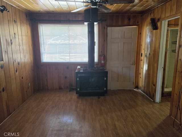 entryway featuring wooden walls, dark wood finished floors, wooden ceiling, ceiling fan, and a wood stove