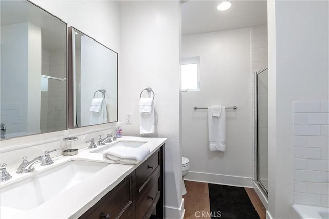 full bathroom with wood finished floors, double vanity, a sink, and an enclosed shower