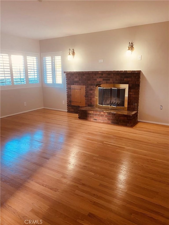 unfurnished living room with a brick fireplace, baseboards, and wood finished floors