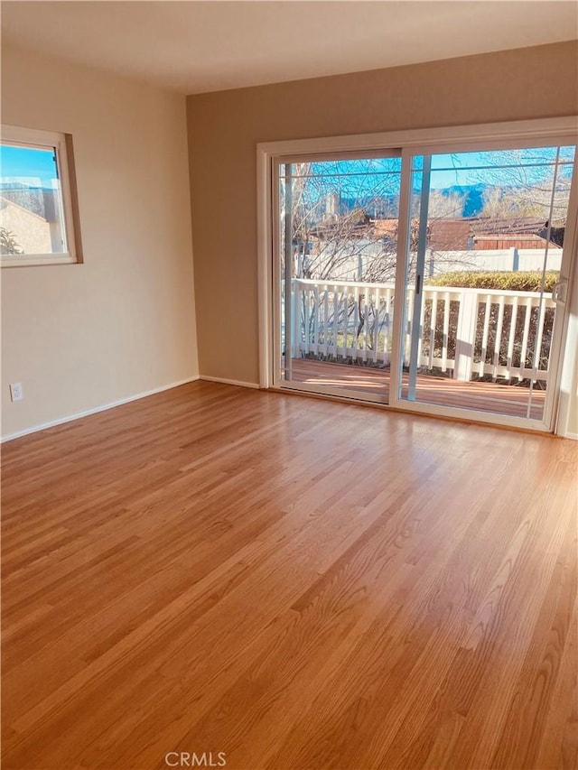 unfurnished room with light wood finished floors, plenty of natural light, and baseboards