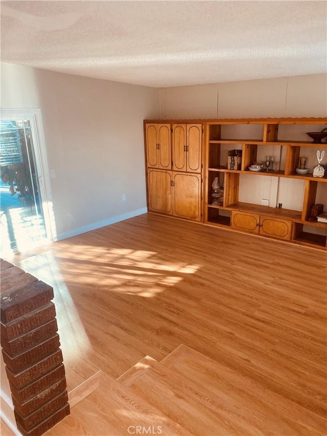 unfurnished living room with light wood-style floors, baseboards, and a textured ceiling