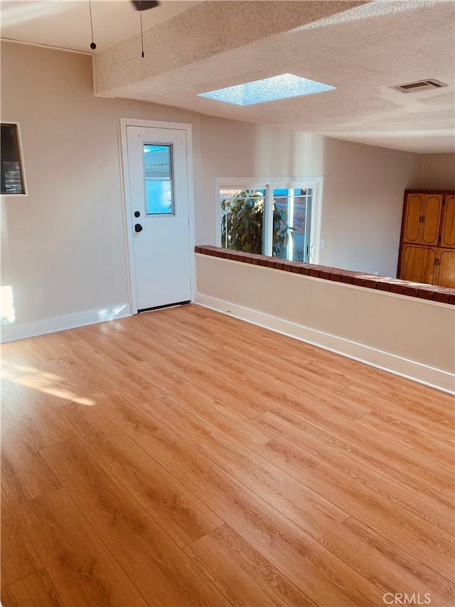 interior space featuring light wood-type flooring, visible vents, a textured ceiling, and baseboards