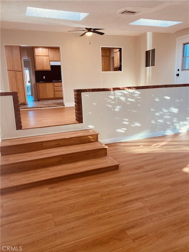 staircase with a textured ceiling, ceiling fan, a skylight, wood finished floors, and visible vents