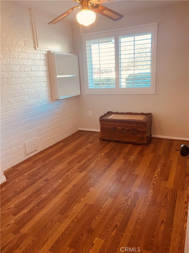 empty room featuring baseboards, ceiling fan, brick wall, and wood finished floors