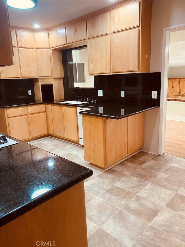 kitchen featuring tasteful backsplash, light brown cabinetry, white dishwasher, a sink, and dark stone countertops