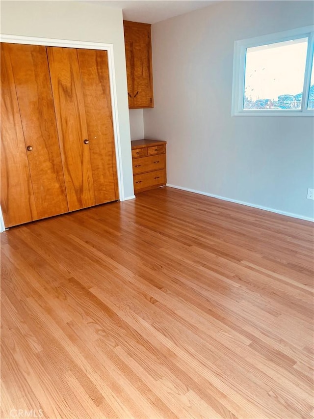 unfurnished bedroom featuring a closet, baseboards, and light wood finished floors