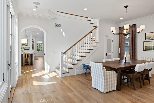 dining space with light wood finished floors, visible vents, arched walkways, stairway, and ornamental molding