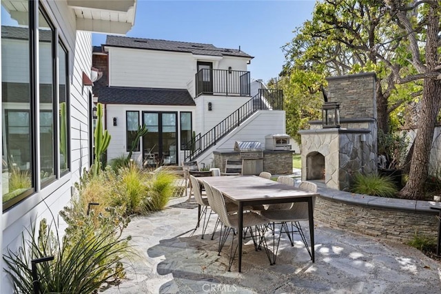 view of patio with stairs, an outdoor stone fireplace, outdoor dining area, and area for grilling