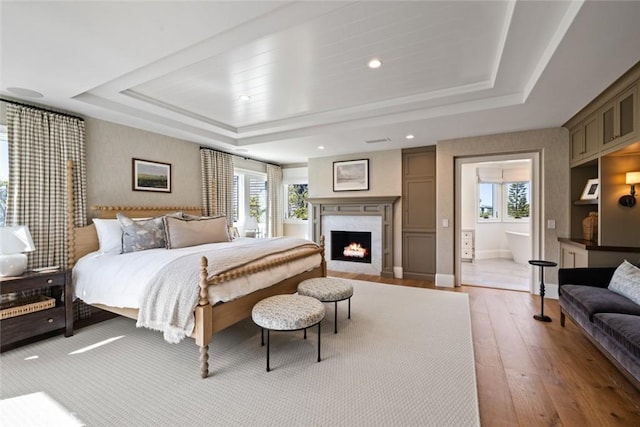 bedroom with a tray ceiling, wood finished floors, a high end fireplace, and recessed lighting