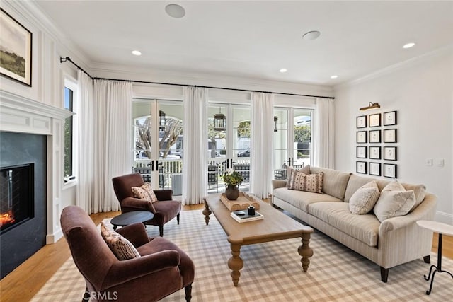 living room with recessed lighting, light wood-style flooring, crown molding, and a glass covered fireplace