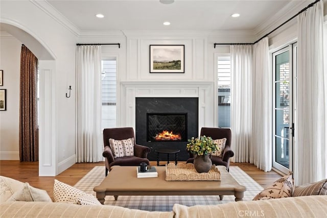 living area featuring arched walkways, light wood finished floors, a premium fireplace, ornamental molding, and baseboards