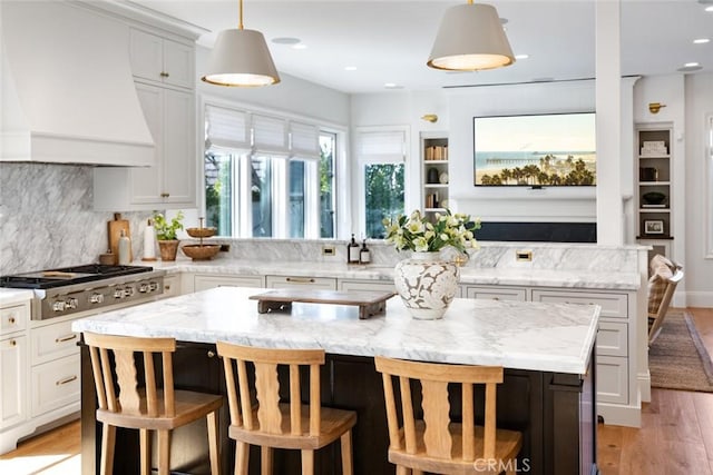 kitchen with a breakfast bar, a center island, stainless steel gas stovetop, hanging light fixtures, and premium range hood