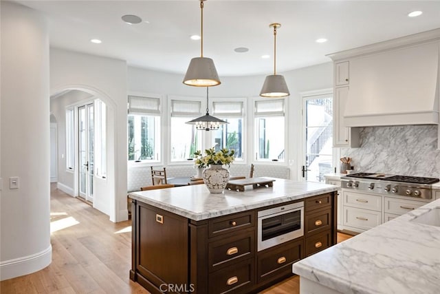 kitchen with arched walkways, white cabinetry, stainless steel gas cooktop, and hanging light fixtures