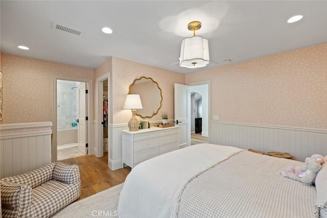 bedroom with light wood-style floors, arched walkways, wainscoting, and wallpapered walls