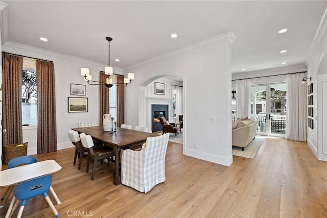 dining space with light wood finished floors, baseboards, a glass covered fireplace, ornamental molding, and an inviting chandelier