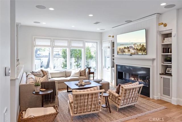 living room featuring recessed lighting, wood finished floors, visible vents, built in features, and a glass covered fireplace