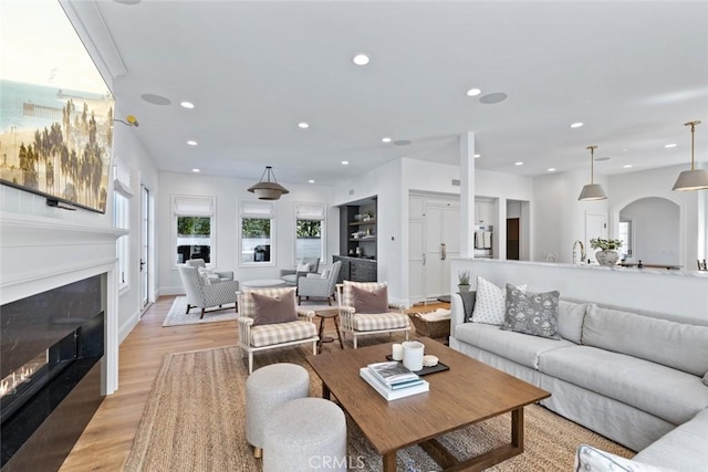 living room with light wood finished floors, recessed lighting, arched walkways, and a glass covered fireplace