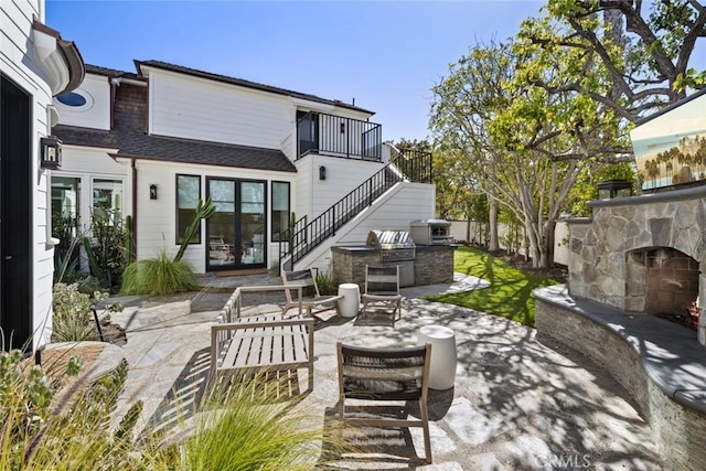 view of patio / terrace featuring stairway, an outdoor stone fireplace, and exterior kitchen