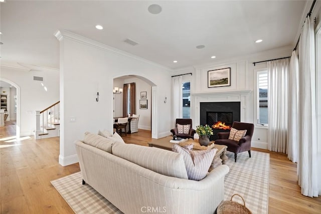 living room featuring arched walkways, a lit fireplace, light wood finished floors, and visible vents