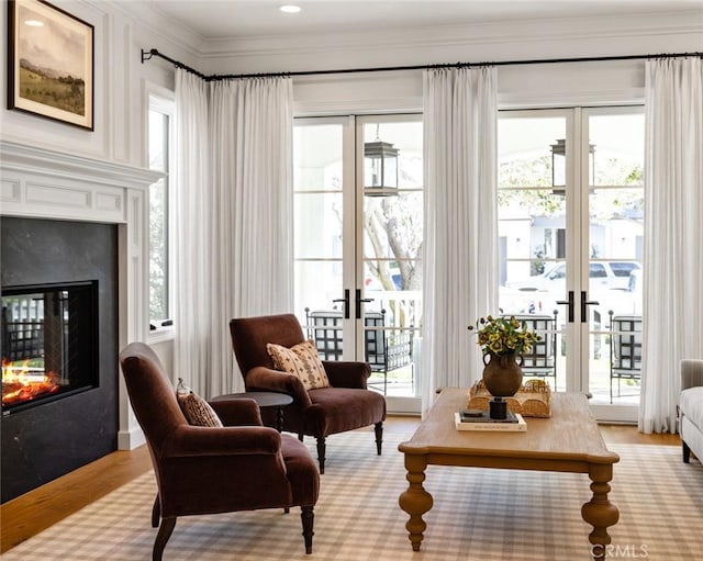 living area featuring light wood-style flooring, a premium fireplace, ornamental molding, and french doors