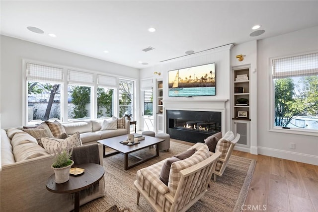 living area with a healthy amount of sunlight, light wood-type flooring, visible vents, and a glass covered fireplace