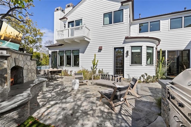 back of property featuring an outdoor stone fireplace, a patio area, a chimney, and area for grilling