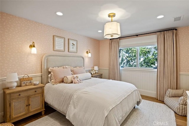 bedroom with light wood-type flooring, wallpapered walls, visible vents, and wainscoting