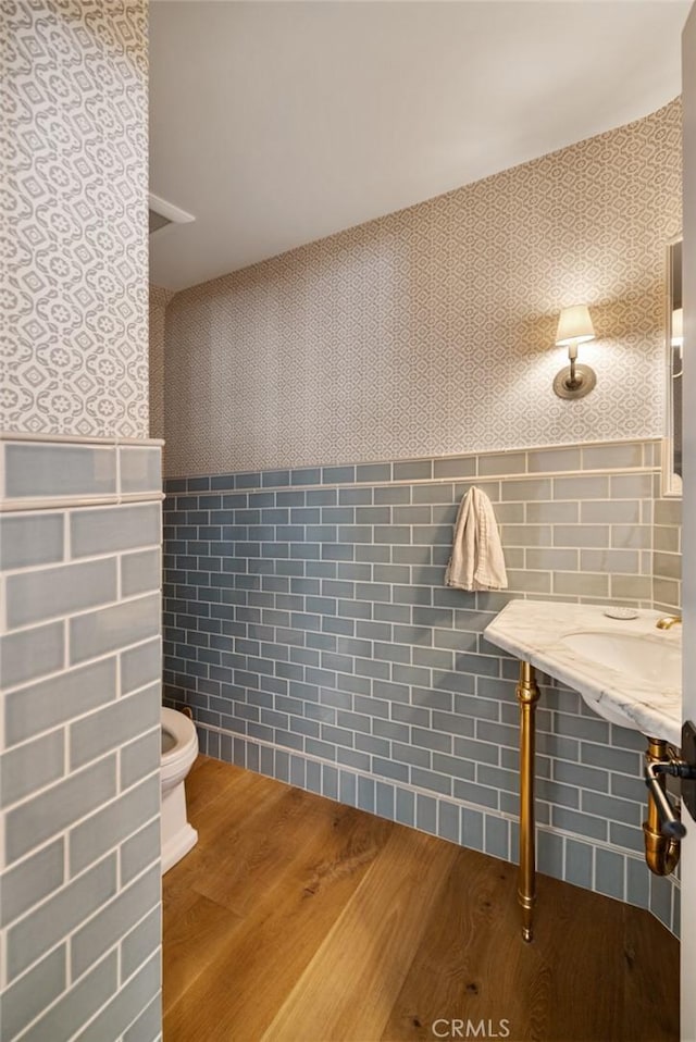 bathroom with toilet, wood finished floors, tile walls, wainscoting, and wallpapered walls