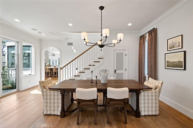 dining space with arched walkways, a notable chandelier, light wood-style floors, baseboards, and crown molding