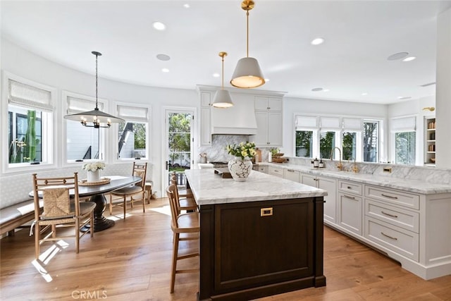 kitchen with light wood-style flooring, white cabinetry, decorative light fixtures, and custom exhaust hood