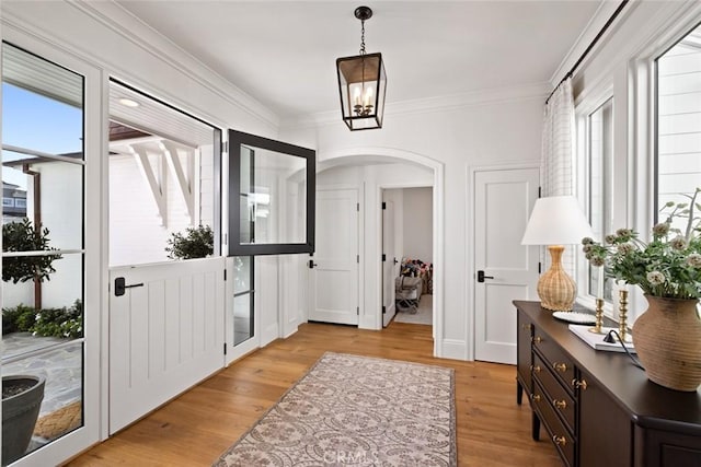 foyer entrance with arched walkways, crown molding, and light wood-style flooring