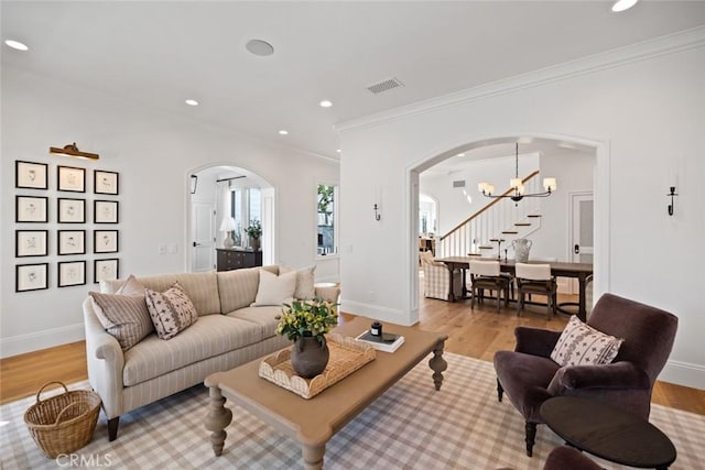 living room featuring arched walkways, ornamental molding, visible vents, and light wood-style floors