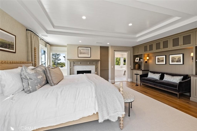 bedroom with recessed lighting, a raised ceiling, a fireplace, and wood finished floors