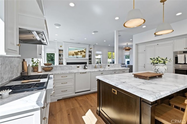 kitchen featuring appliances with stainless steel finishes, a kitchen breakfast bar, light stone counters, decorative light fixtures, and a peninsula