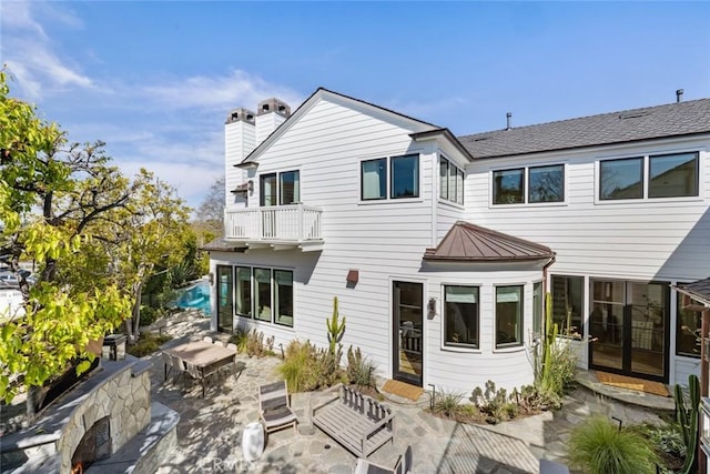 rear view of property featuring a chimney, a standing seam roof, a patio area, metal roof, and a balcony