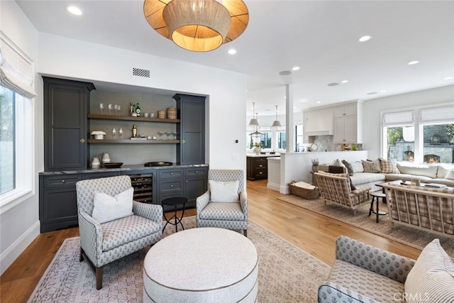 living room featuring light wood-type flooring, wine cooler, a bar, and recessed lighting