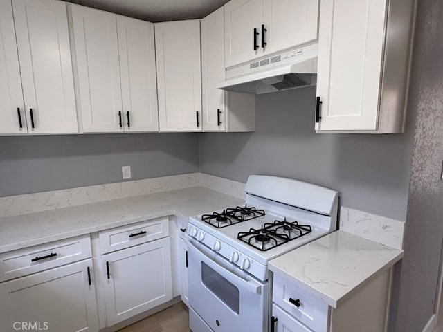 kitchen with under cabinet range hood, white range with gas cooktop, white cabinetry, and light stone counters