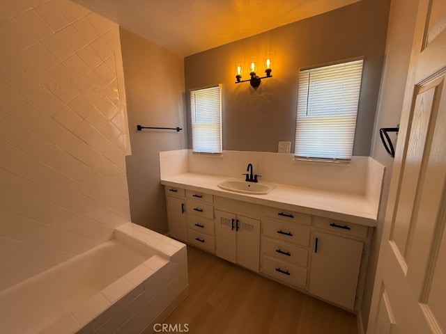 bathroom with a relaxing tiled tub, vanity, and wood finished floors