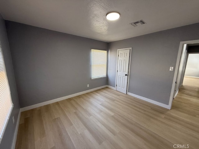 empty room with light wood-style floors, visible vents, a textured ceiling, and baseboards