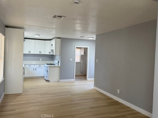 kitchen with light wood finished floors, white gas range, light countertops, visible vents, and white cabinetry