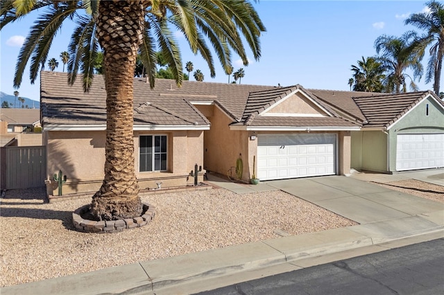 view of front of house featuring a garage, concrete driveway, a tile roof, fence, and stucco siding