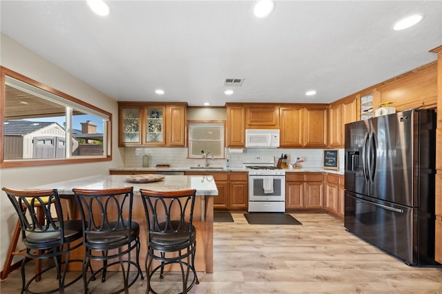 kitchen with white appliances, glass insert cabinets, light countertops, a kitchen bar, and a sink